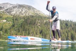 Beginner standing on a wide all-around stand-up paddle board on a calm lake