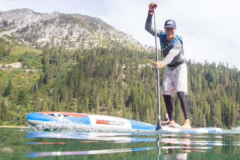 Beginner standing on a wide all-around stand-up paddle board on a calm lake