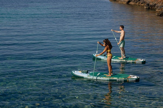 Paddle board, SUP paddle, leash, and life vest laid out on a beach