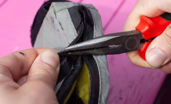 Using pliers to repair a worn zipper slider on a jacket while camping