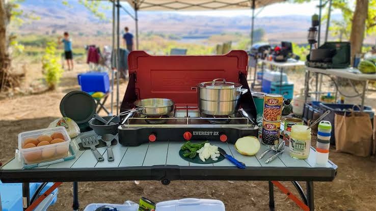 Camp stove and cookware set up on a camp table outdoors