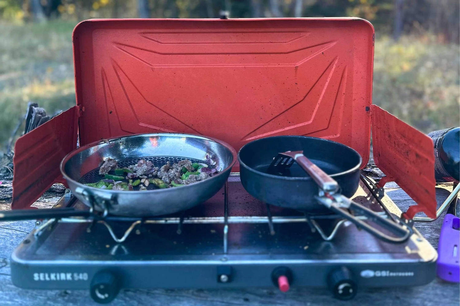 Two-burner propane camp stove cooking outdoors, illustrating how to pick a camping